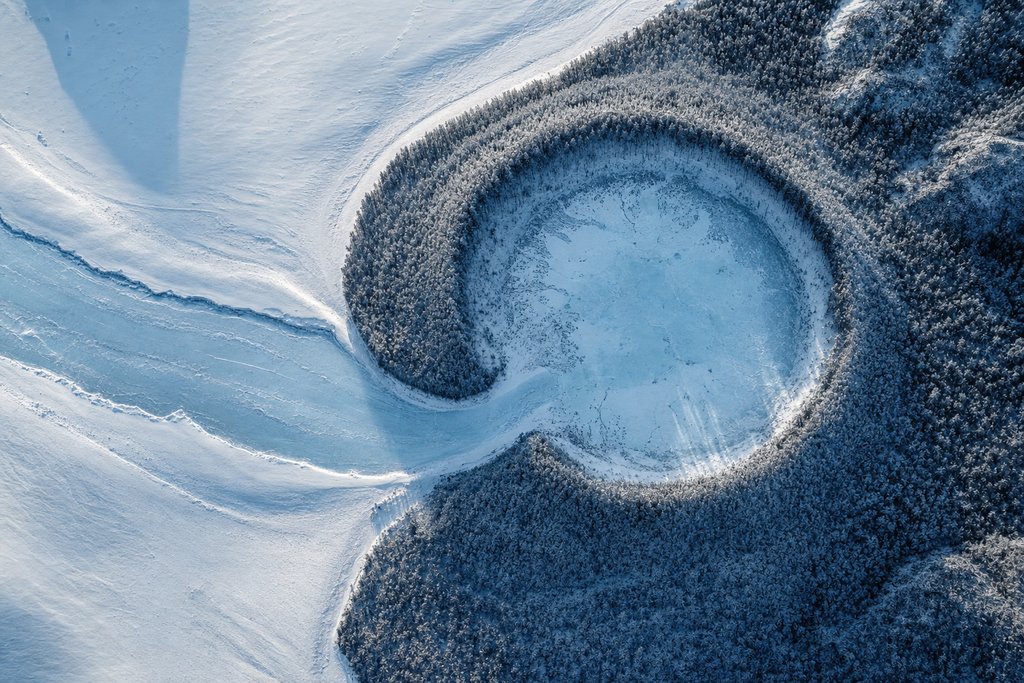 Aerial view of a frozen river bending sharply and ending in a closed basin ringed entirely by snow-covered forest — the plate for where the complaint chain stops in this province