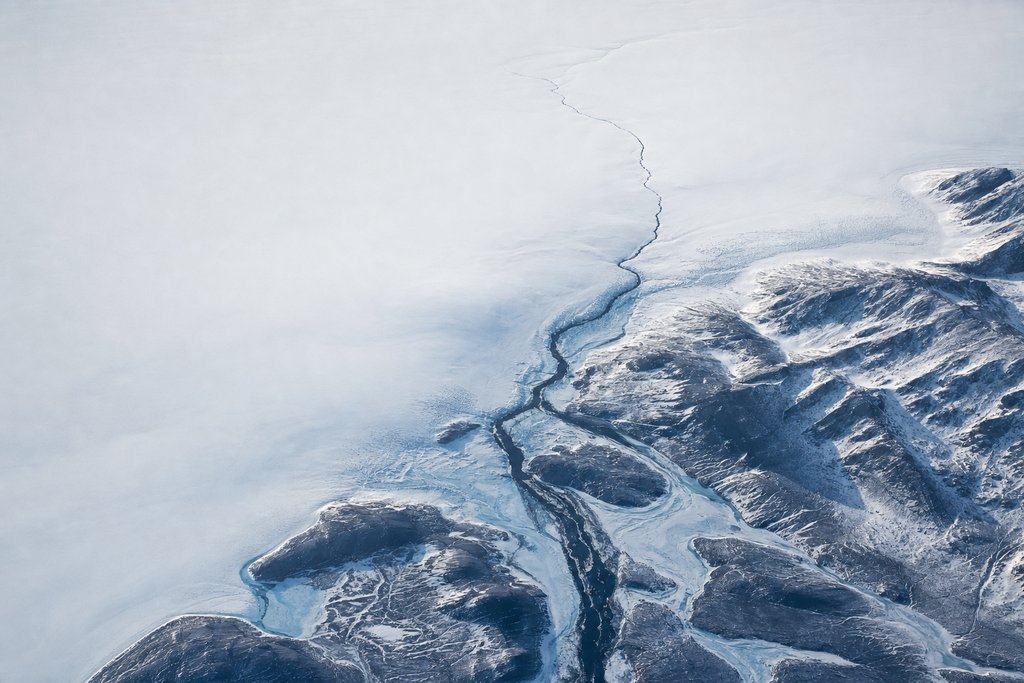 Aerial view of a wide frozen river narrowing to a single dark thread and disappearing beneath an unbroken snowfield — the plate for where the complaint chain stops in this province