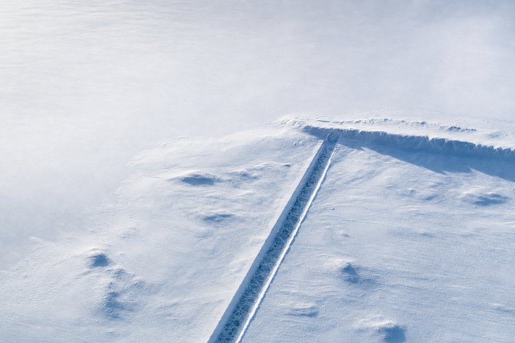 Aerial view of a perfectly straight frozen drainage channel crossing flat prairie snow and stopping at a raised bank — the plate for where the complaint chain stops in this province