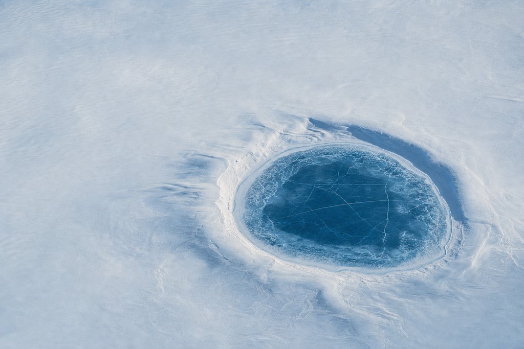 Aerial view of a single isolated frozen lake at the centre of an immense empty snow plain, with no inflow and no outflow — the plate for where the complaint chain stops in this province