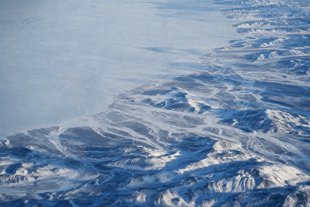 Aerial view of snow-covered foothills meeting open prairie, a braided river valley cutting pale channels through the white — the plate for the Alberta safety index