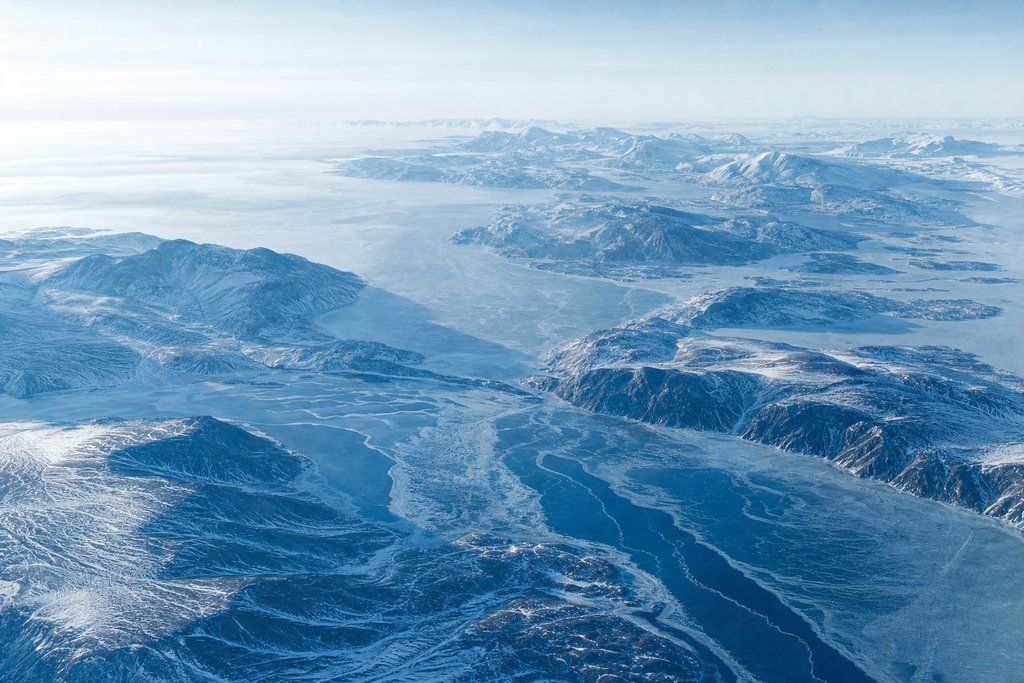 Wide high-altitude aerial panorama of a cold northern landscape, layered ridgelines receding into pale distance — the plate for the national comparison
