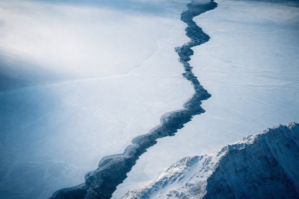 Aerial view of a frozen lake split across its full width by one dark meltwater seam, the ice on both sides identical in texture and tone — the plate for affiliate disclosure page
