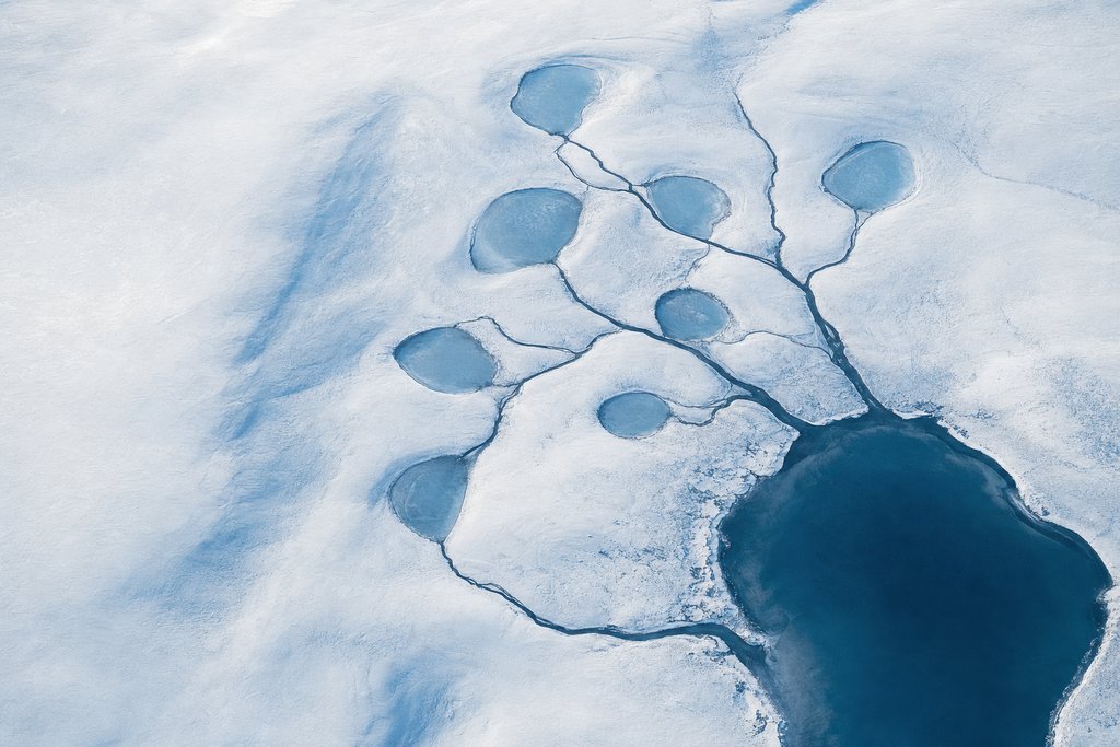 Aerial view of seven small frozen ponds of similar shape scattered across a snow plain, all fed by one branching dark channel from a single larger lake — the plate for casino rewards in the licences section