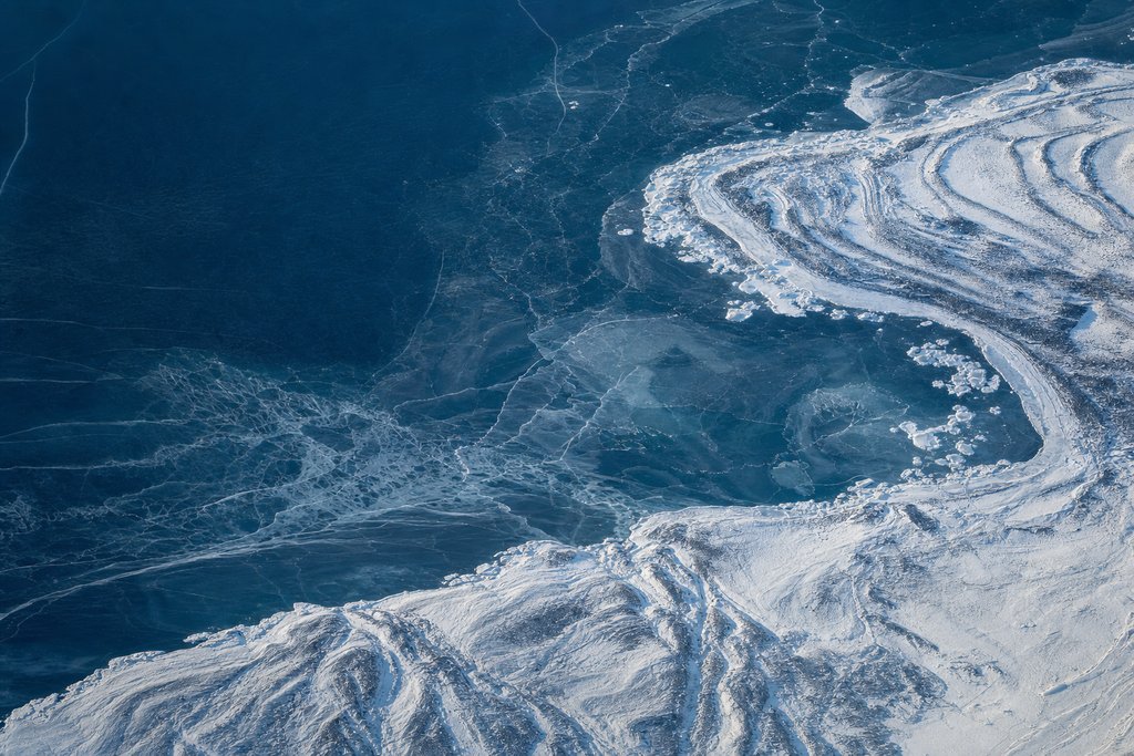 Aerial view of a thin fragile sheet of newly formed ice over dark water, translucent enough that the depth shows through it — the plate for curacao in the licences section