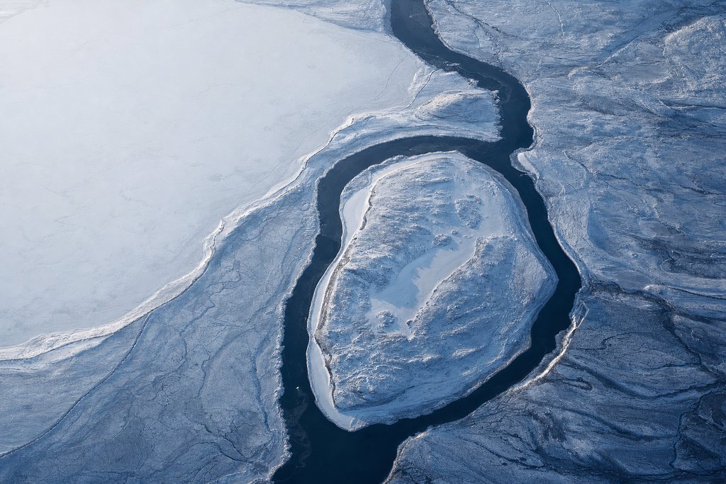 Aerial view of a frozen river island with a distinct raised shoreline, the dark channel dividing cleanly around it and rejoining beyond — the plate for kahnawake in the licences section