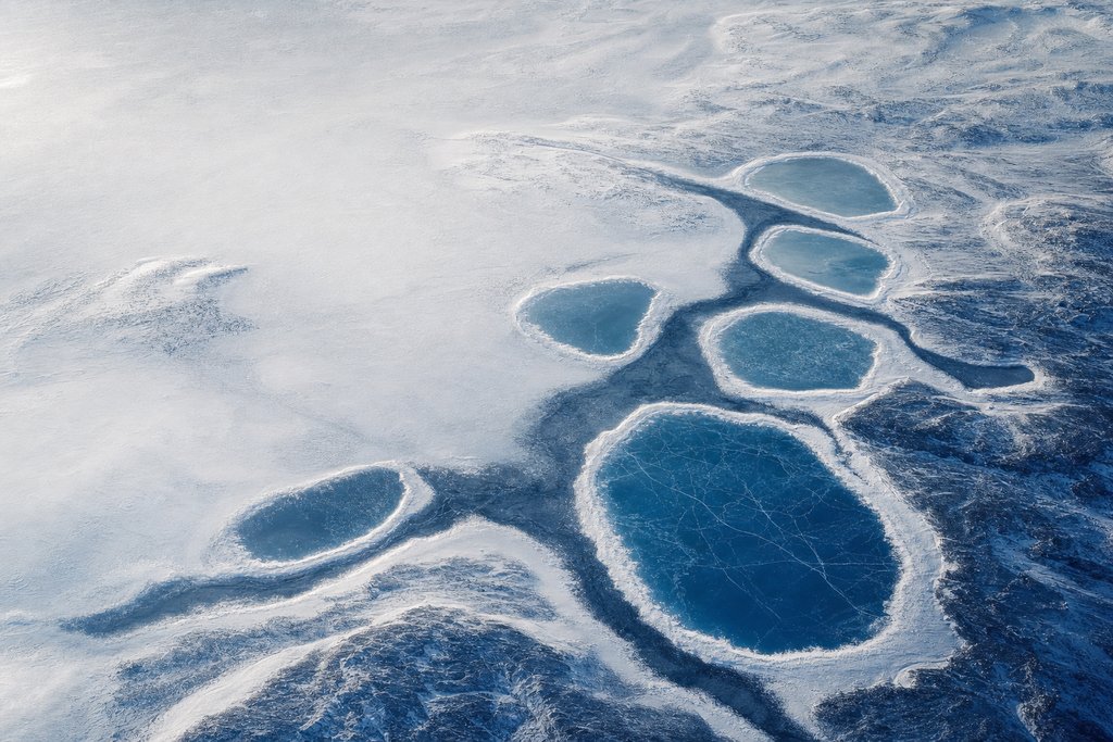 Aerial view of several separate frozen surface pools that share one dark subsurface channel, faintly visible running beneath the ice between them — the plate for who owns canadian casinos in the licences section