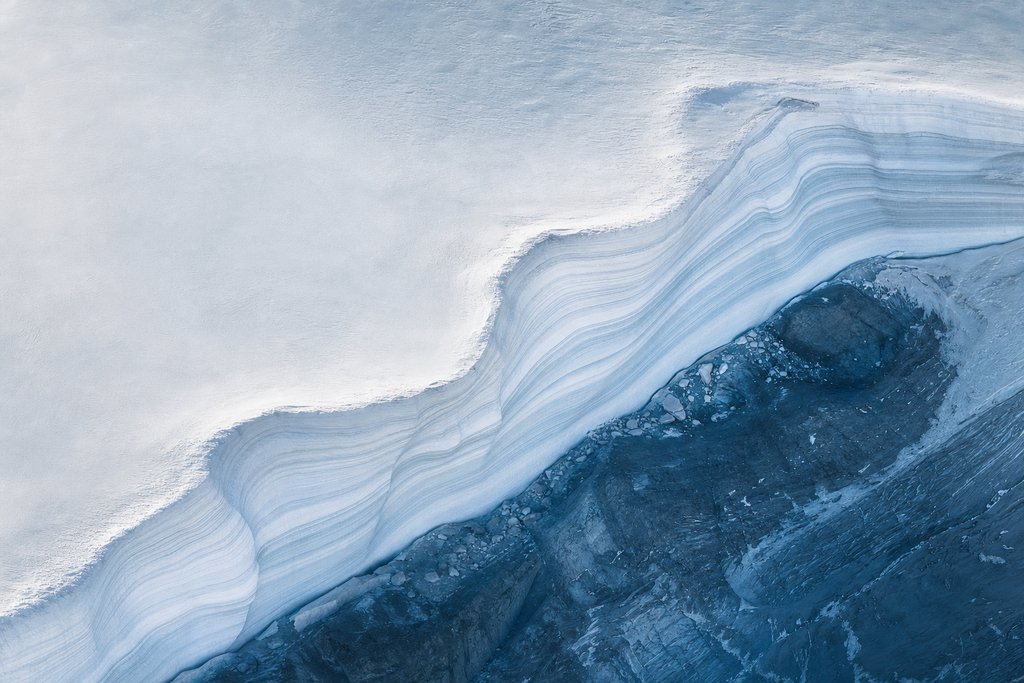 Aerial view of a snowbank cut open to reveal many fine distinct horizontal layers of compacted snow, each a slightly different shade of white — the plate for our sources page