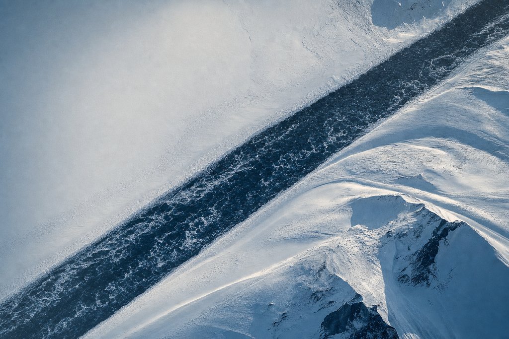 Aerial view of a wide dark meltwater channel running fast and perfectly straight across a snowfield with clean unobstructed banks — the plate for fast payout ontario in the payouts section
