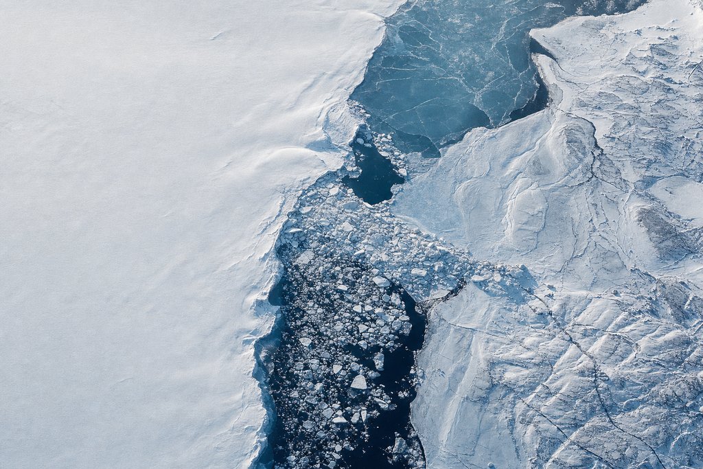 Aerial view of a dark channel blocked mid-course by a jam of piled broken ice, the water visibly backed up behind it — the plate for unpaid winnings in the payouts section