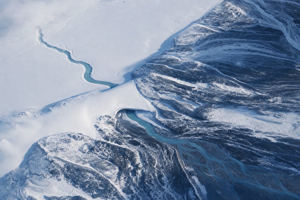 Aerial view of a river channel disappearing beneath a long snow bridge and re-emerging much further downstream — the plate for why payouts are delayed in the payouts section