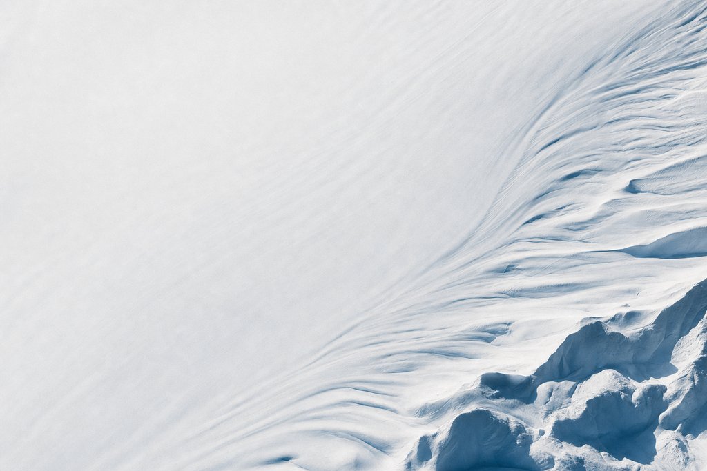 Aerial view of an entirely unmarked expanse of fresh snow carrying only a single set of faint wind lines and nothing else — the plate for privacy page