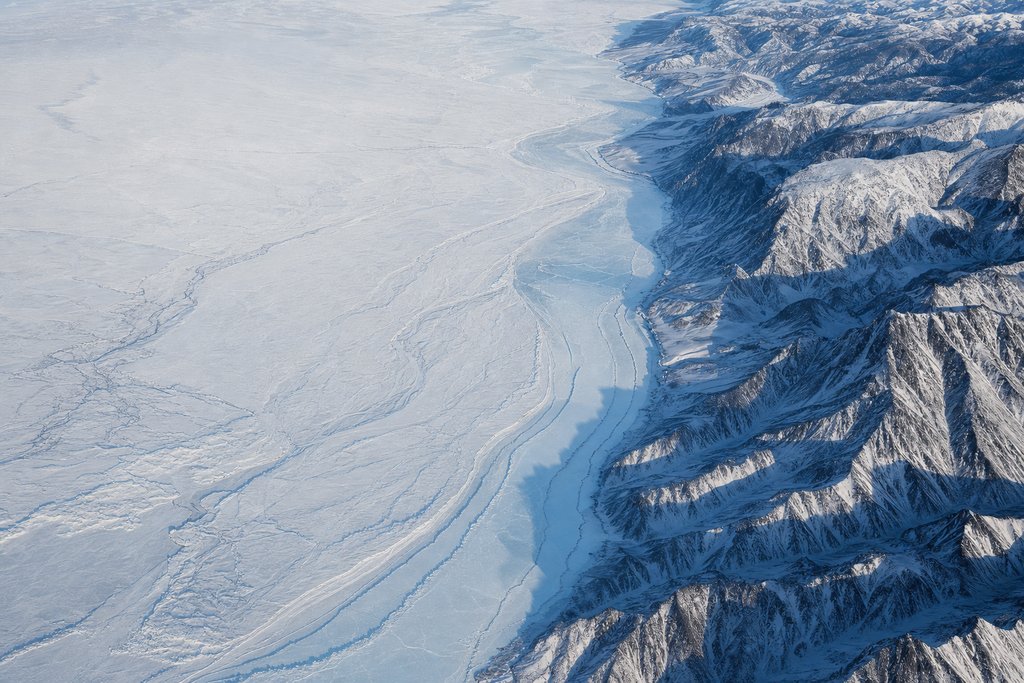 Aerial view of a broad frozen river in a deep snow-covered valley, one bank steep and rocky, the other a low flat plain — the plate for Espacejeux, the provincial site scored on the same rubric