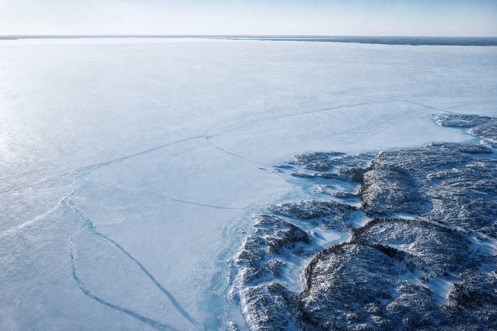 Aerial view of an enormous frozen lake filling most of the frame, its far shore only a thin dark line at the horizon — the plate for OLG.ca, the provincial site scored on the same rubric