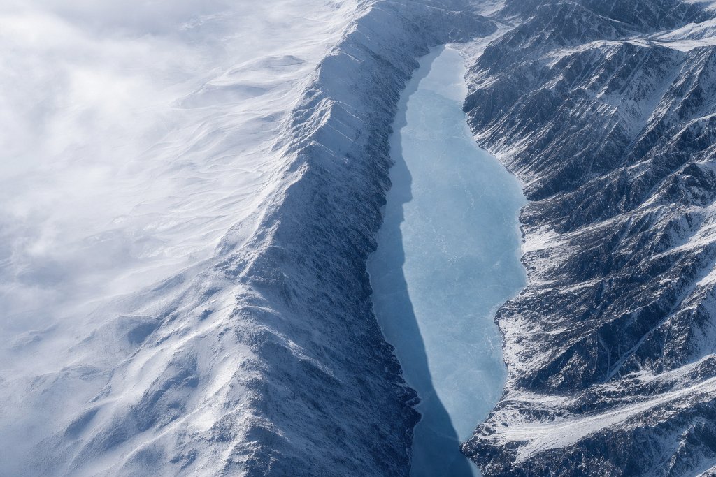 Aerial view of a narrow frozen mountain lake held between two very steep snow-covered ridges — the plate for PlayNow.com, the provincial site scored on the same rubric