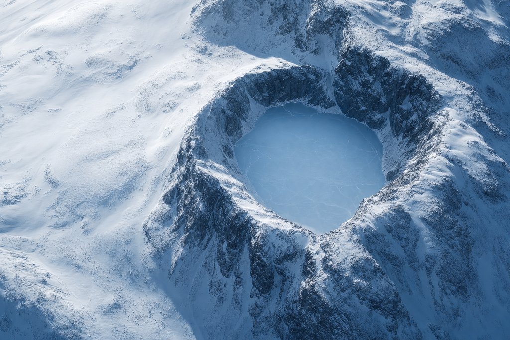 Aerial view of a small frozen lake completely enclosed by a steep unbroken wall of snow-covered rock, with no visible approach — the plate for account security in the safer gambling section