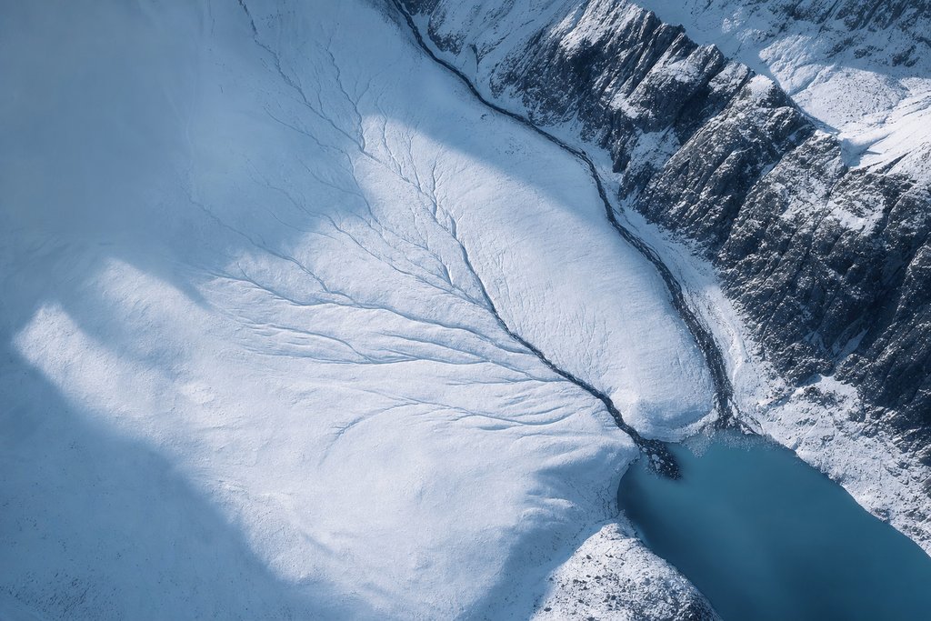Aerial view of several faint natural drainage lines on a snow slope all converging into one clear dark channel — the plate for where to get help in the safer gambling section