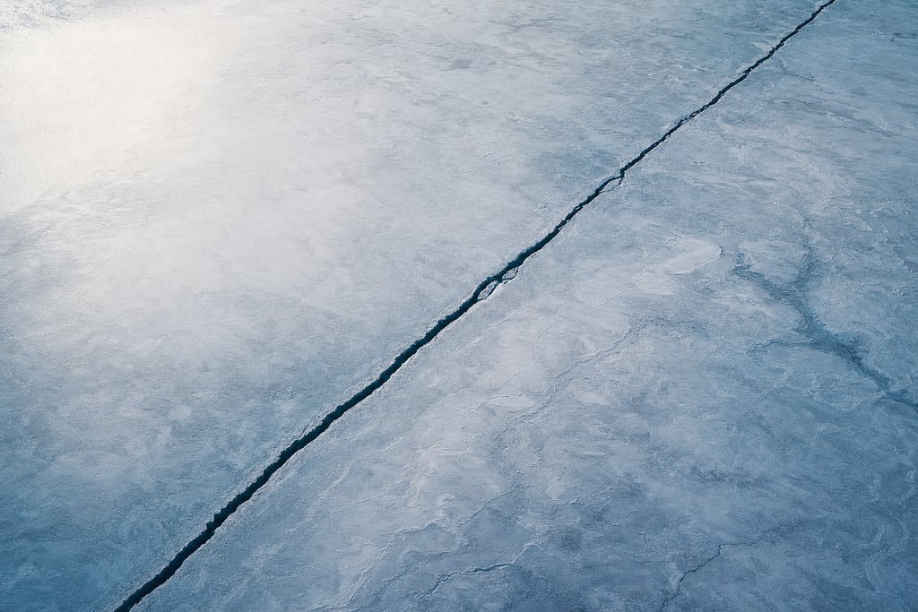 Aerial view of a flat expanse of lake ice carrying one long straight crack running corner to corner and nothing else — the plate for terms page