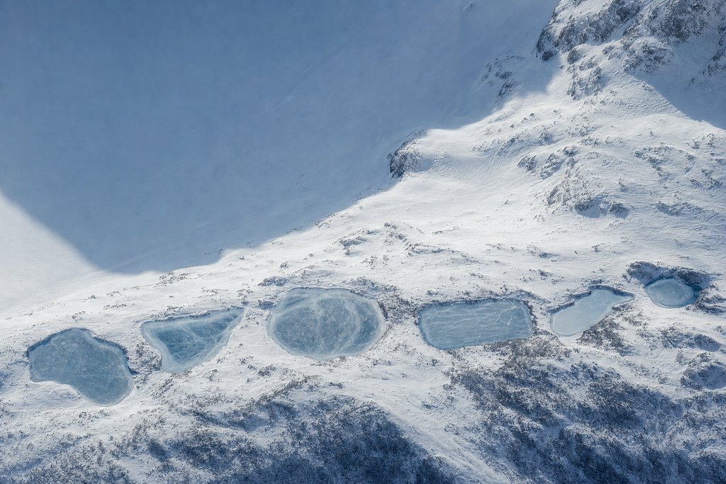Aerial view of six small frozen tarns of clearly different shape set in a row along a snow-covered bench — the plate for the tools section