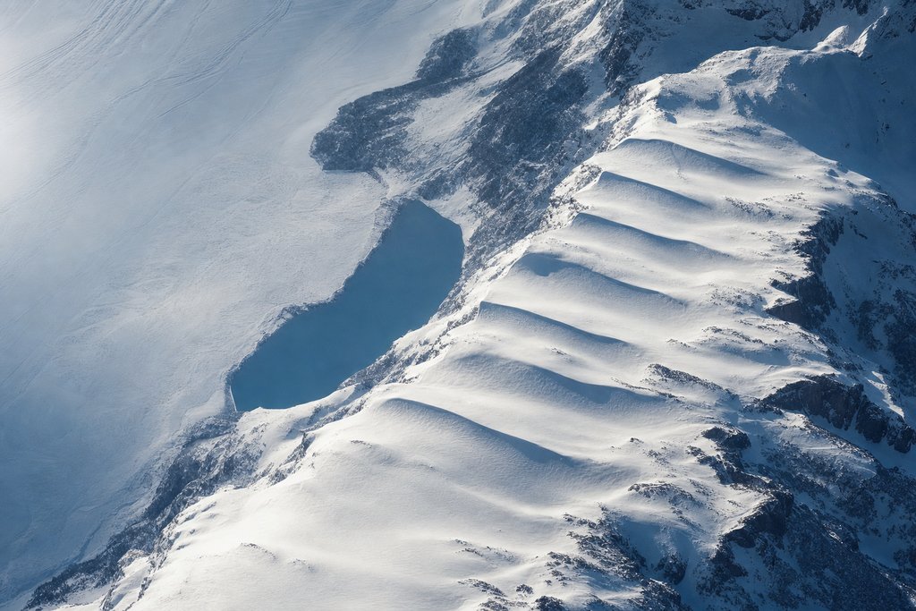Aerial view of a long snow slope descending in a series of regular shallow steps, each step slightly lower than the last — the plate for the cost-of-play calculator