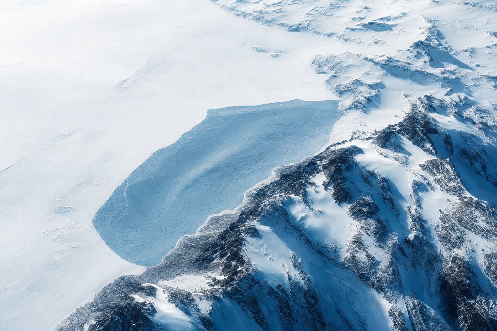 Aerial view of a snowfield in which one area of ice is visibly different in tone and texture from everything around it, its boundary sharp and clean — the plate for the operator legitimacy check