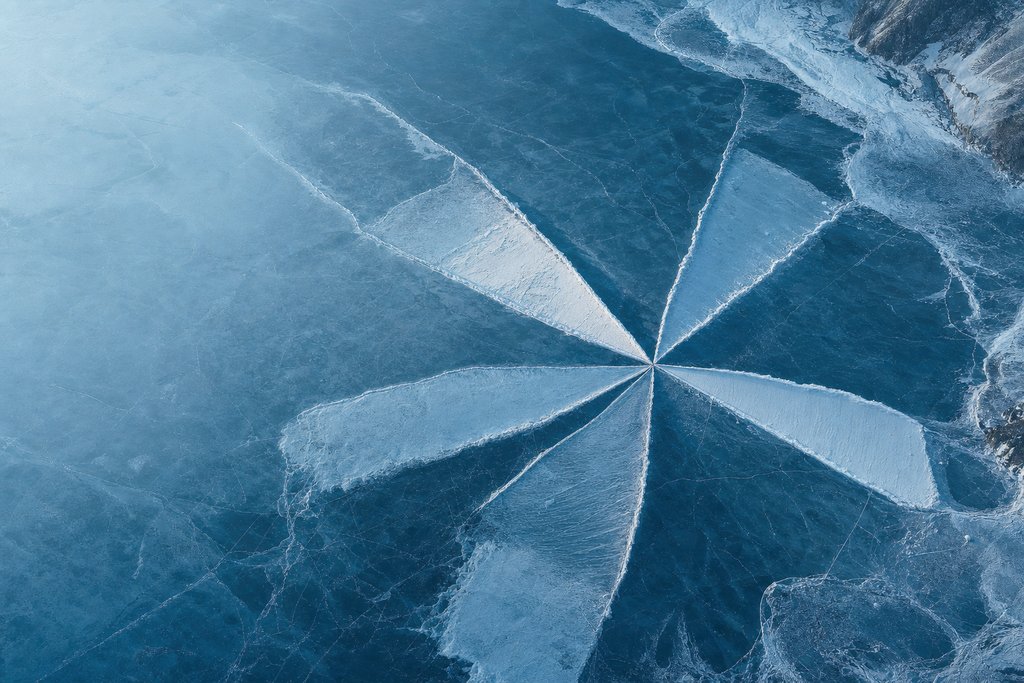 Aerial view of a frozen lake where six wedge-shaped ice formations radiate from a single centre, each one a different length — the plate for the safety score explorer