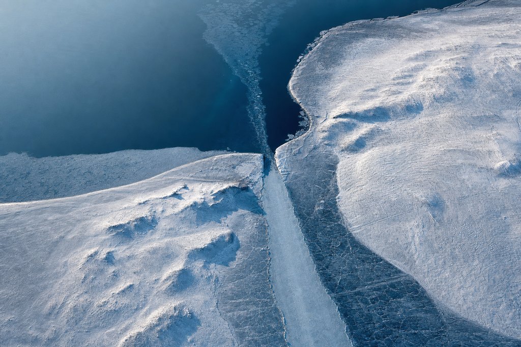 Aerial view of a frozen channel with a clear straight approach passing through one narrow gate between two ice shoulders, open water beyond — the plate for the withdrawal readiness check