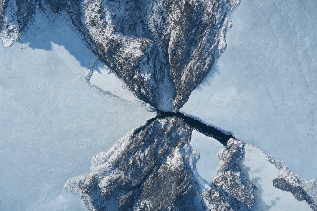 Aerial view of a wide frozen expanse squeezed through one narrow dark gap between two rock headlands, opening out again beyond it — the plate for where a withdrawal is held up