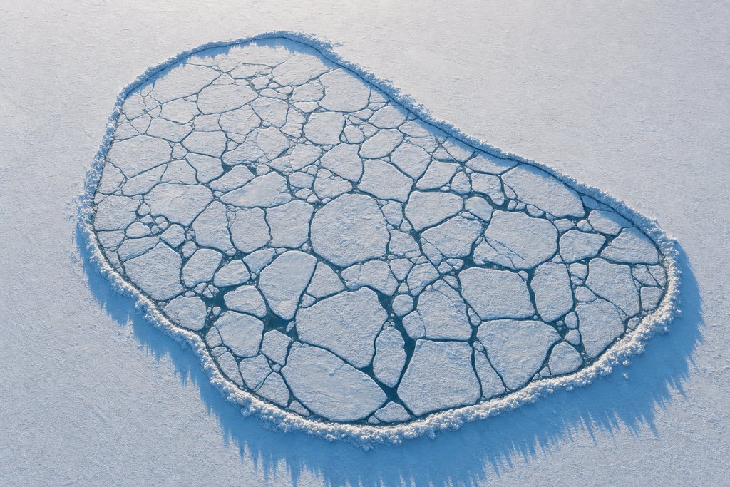 Aerial view of a frozen lake broken into many separate pale ice floes, all enclosed within a single unbroken ridge of raised pressure ice — the plate for why protection is compared by province