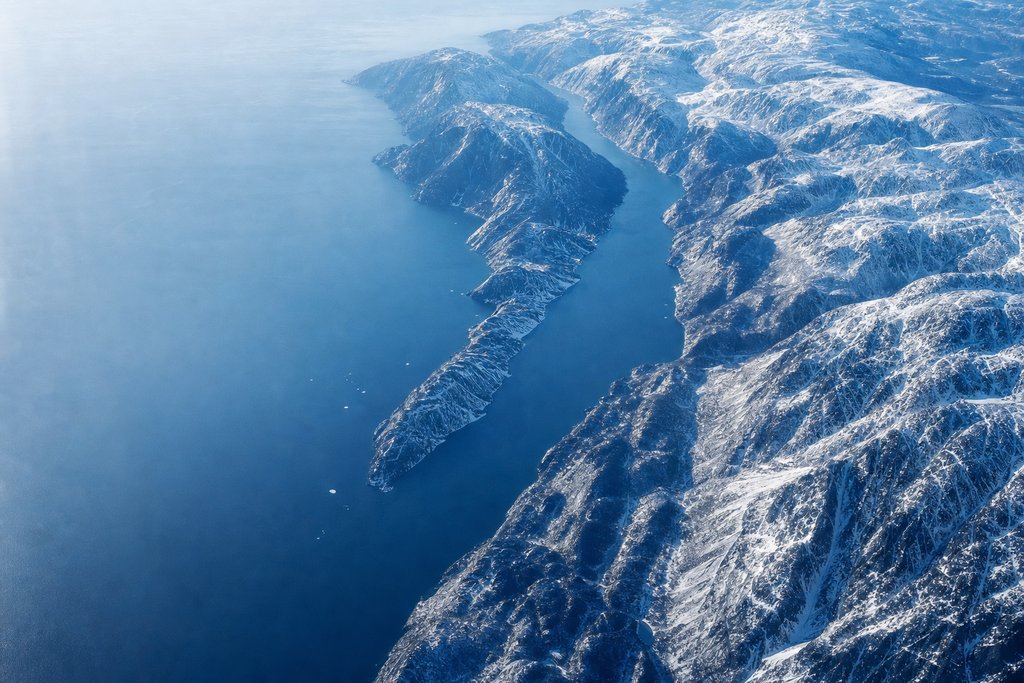 Aerial view of a deep coastal fjord between steep snow-covered mountains, dark water far below — the plate for the British Columbia safety index
