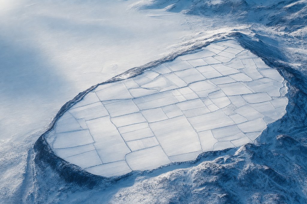 Aerial view of a broad snowfield divided into many separate pale rectangular panels by fine dark seams, the whole field held inside one continuous darker boundary ridge — the plate for the Ontario operator register